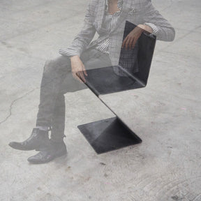 Eine Person sitzt auf einem Freischwinger aus rohem Flachstahl auf Betonboden